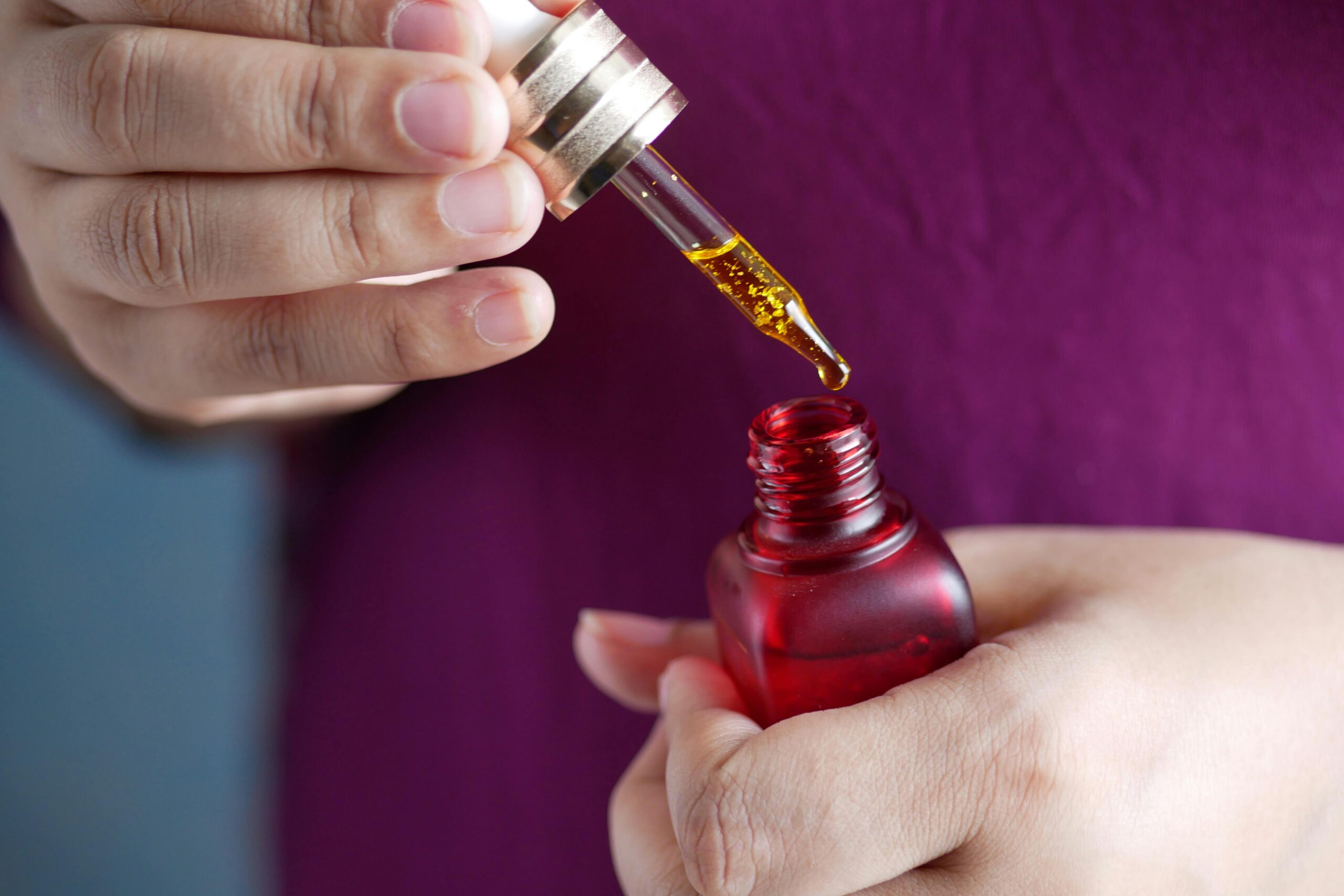 Detailed image of hands using a dropper with a red glass bottle. Perfect for skincare and beauty themes.